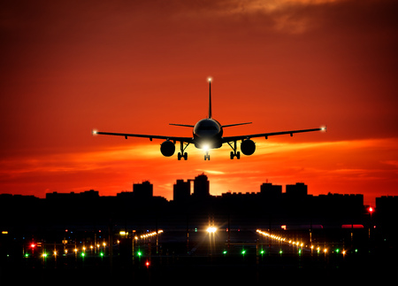 Passengers commercial airplane landing on runway with dramatic sunset sky. Modern cityscape with silhouettes of skyscrapers on background. Concept of fast travelの写真素材