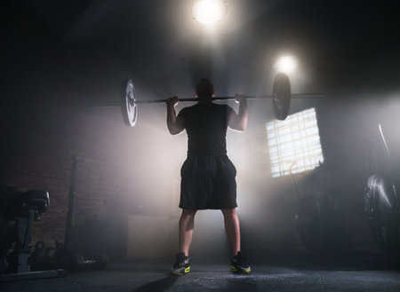 Weightlifter flipping two-handed dumbbell and preparing for workout in gym interior. Cinematic mood...