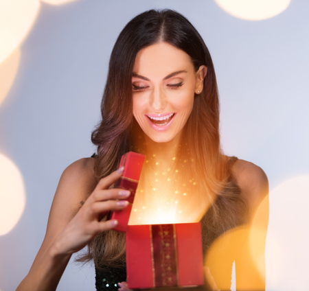 Beautiful brunette young woman holding gift box and making surprise expression. Concept of winter, Christmas and surprise.の写真素材