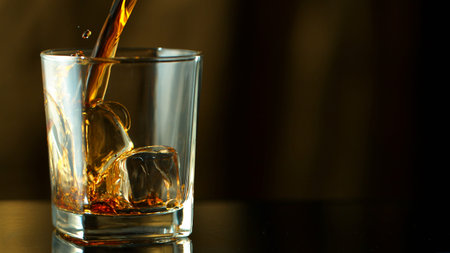 Pouring whiskey into glass in freeze motion. Free space for text, dark background.