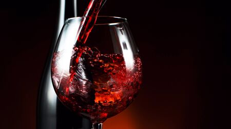 Detail of pouring red wine into glass, dark gradient background. Free space for textの写真素材