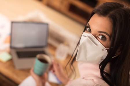 Young woman in home quarantine, wearing face mask protection.