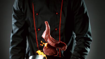 Closeup of chef throwing raw beef steaks from wok pan in fire. Fresh asian food preparation on dark background.の写真素材