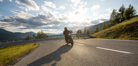 Motorcycle rider on the mountain road, wide format. Dramatic sunset sky