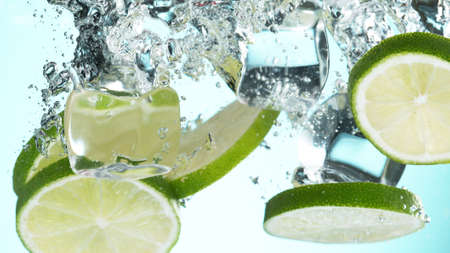 Fresh lime dropped into water with splash and ice cubes. Studio shot with clear background.の写真素材