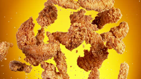 Freeze motion of flying pieces of fried chicken pieces on golden background. Concept of levitating food.の写真素材