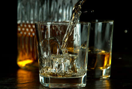 Freeze motion of falling ice cube into whiskey, isolated on black background.の写真素材