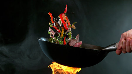 Closeup of chef throwing salmon pieces with asian mix from wok pan in fire. Fresh asian food...