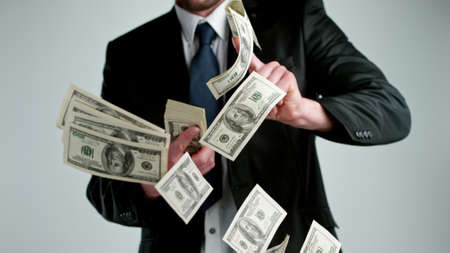 Close-up of screaming businessman with flying dollars banknotes isolated over gray backgroundの写真素材