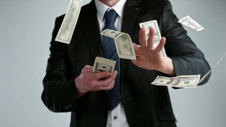 Close-up of screaming businessman with flying dollars banknotes isolated over gray backgroundの写真素材