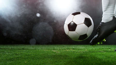 Soccer ball on grass with dark background and lights, placed on center of image.の写真素材