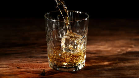 Detail of pouring whiskey into glass. Served on old wooden table.の写真素材