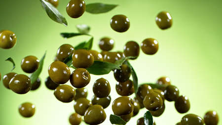 Freeze motion of flying green olives with leaves, isolated on green background.の写真素材
