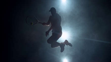 Dramatic tennis player silhouette jumping up in the air. Silhouette with smoke on background, dark wallpaper scene, artistic feeling.の写真素材