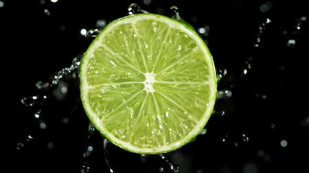 Slice of lime with water splashes on black background. Isolated studio shot, fresh fruit background.の写真素材