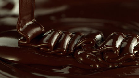 Close-up of pouring stream of melted chocolate, creating curly shapes.