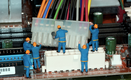 Motherboard Repair - Miniature construction worker figurines posed as if working on a computer motherboard.の写真素材