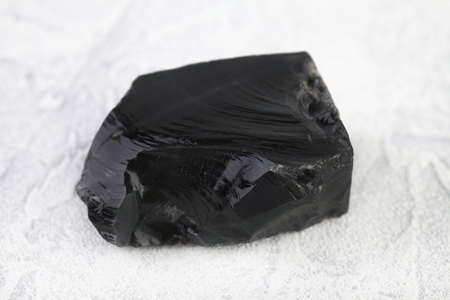 Natural rock - Obsidian, volcanic glass mineral stone from Djalaber, Armenia on white cement background.の写真素材