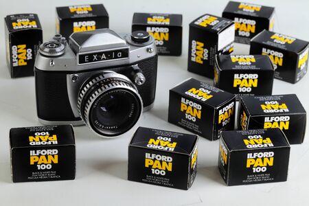The old German 35 mm SLR film camera Exa-1a with Carl Zeiss lens Tessar 2,8 50, released 1974 in East Germany on a white cement background with film packings lford.のeditorial素材
