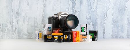 The old Japan 35 mm SLR film camera Canon EOS ELAN IIe 50e with 135 mm Canon lens, released 1995 with packings photographic films on white cement background.のeditorial素材