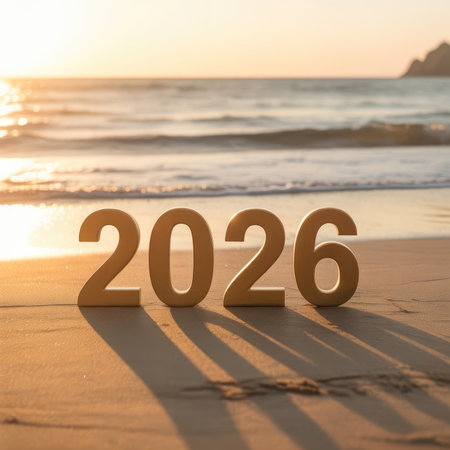 The year 2026 is displayed in large wooden numbers on a sandy beach at sunset, with gentle waves in the background.の素材
