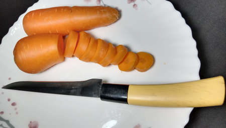 Fresh and delicious and healthy carrot pieces and a knife on plateの写真素材