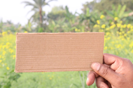 brown colored sign card on hand with mustard farm for any textの写真素材