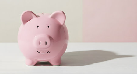 A charming pink ceramic piggy bank with a happy smile sits on a white surface, casting a soft shadow.の素材