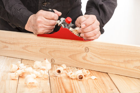 Middle aged carpenter planing the surface of a plank of wood