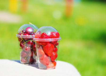 Strawberry and cherry berries in plastic cup in a summer parkの写真素材