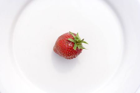 Single juicy strawberry on a white circular plate, view from overhead, landscape formatの写真素材
