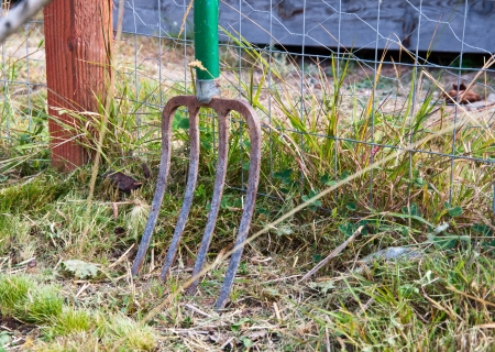 Rusty old pitchfork leaning against a fenceの写真素材
