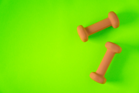 Fitness equipment with womens yellow orange weights/ dumbbells isolated on a neon lime green background with copyspace (aka empty text space).の写真素材