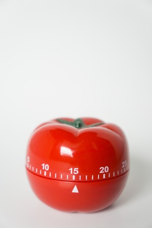 Close up view of mechanical tomato shaped kitchen clock timer for cooking and studying. Used for pomodoro technique for time and productivity management. Isolated on white background, at 15 minutes.の写真素材