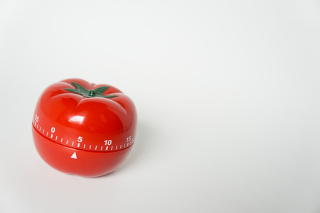 Close up view of mechanical tomato shaped kitchen clock timer for cooking and studying. Used for pomodoro technique for time and productivity management. Isolated on white background, at 5 minutes.の写真素材