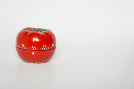 Close up view of mechanical tomato shaped kitchen clock timer for cooking and studying. Used for pomodoro technique for time and productivity management. Isolated on white background, at 30 minutes.の写真素材