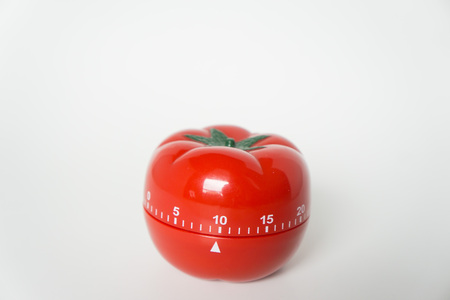 Close up view of mechanical tomato shaped kitchen clock timer for cooking and studying. Used for pomodoro technique for time and productivity management. Isolated on white background, at 10 minutes.の写真素材