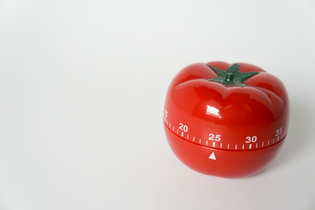 Close up view of mechanical tomato shaped kitchen clock timer for cooking and studying. Used for pomodoro technique for time and productivity management. Isolated on white background, at 25 minutes.の写真素材