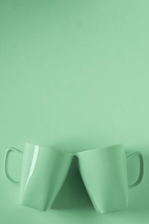 2 monochromatic green coffee mugs on green background clinking in cheers with blank empty room space for text, copy, or copyspace. Modern top view concept of two cups with solid background backdrop.の写真素材
