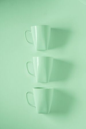 3 monochromatic green coffee mugs lined up in a row on green background with blank empty room space for text, copy, or copyspace. Modern top view concept of three cups with solid background backdropの写真素材