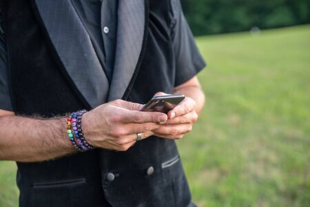 Alternative married white caucasion male man in all black and rainbow bracelets while texting on his mobile cell phone. Pride for lgb, lgbt, or lgbtq.の写真素材