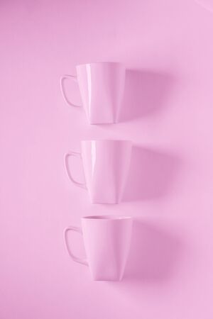 3 monochromatic pink coffee mugs lined up in a row on pink background with blank empty room space for text, copy, or copyspace. Modern top view concept of three cups with solid background backdropの写真素材