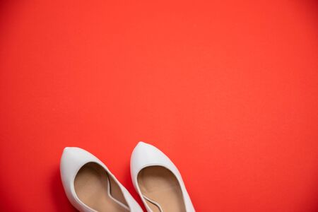 White high heeled shoes on red background - top view concept - blank empty room space for text or copy. Suitable for holidays like Valentine's or Christmas. Classic fashion. Heels pointing leftの写真素材