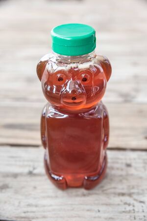 Healthy organic natural sweetener, raw honey - from bees. Golden brown liquid in bear shaped bottle with green cap. Isolated on solid wooden background with blank empty room space for text or copy.の写真素材