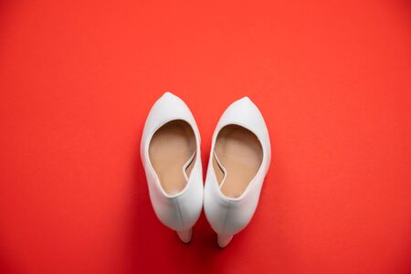 White high heeled shoes on red background - top view concept - blank empty room space for text or copy. Suitable for holidays like Valentine's or Christmas. Classic dress up fashion. Heels pointing upの写真素材