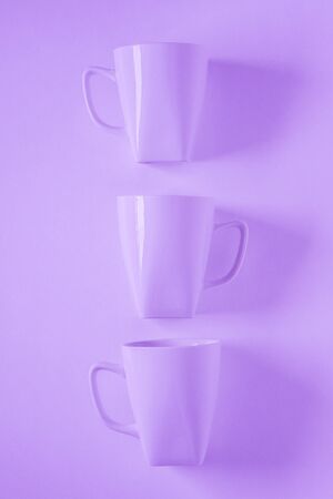 3 monochromatic purple coffee mugs lined up in a row on violet background with blank empty room space for text, copy, or copy space. Modern top view concept of three cups, solid background backdropの写真素材