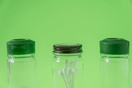 3 Glass spice jars on lime green background with blank empty room space for text or copy. Three kitchen bottles recycled and reused to store cotton swabs bathroom essentials. Recyclable junk garbage.の写真素材