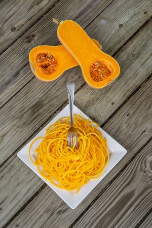 Top view of healthy butternut squash noodles with fork stuck in pasta. Vegan, gluten free, and low carb health food trend for keto diets. Orange yellow in color on wooden background and white plate.の写真素材