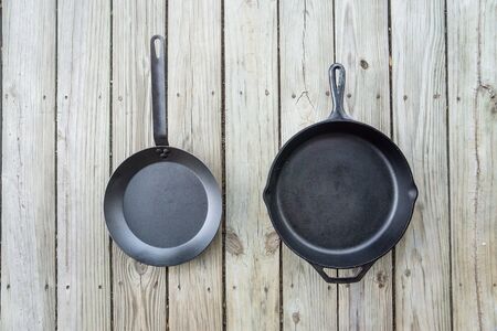Traditional cast iron vs carbon steel versus teflon cooking options - blank empty room for text or copy space. Two cookware pieces - kitchen stove to oven to campfire. Durability test. Head to head.の写真素材