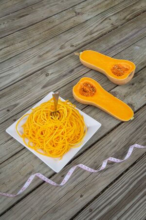 Butternut squash noodles with fork and measuring tape on wooden background. Healthy low carb pasta - new health food trend with vegetable noodle. Grain free.の写真素材